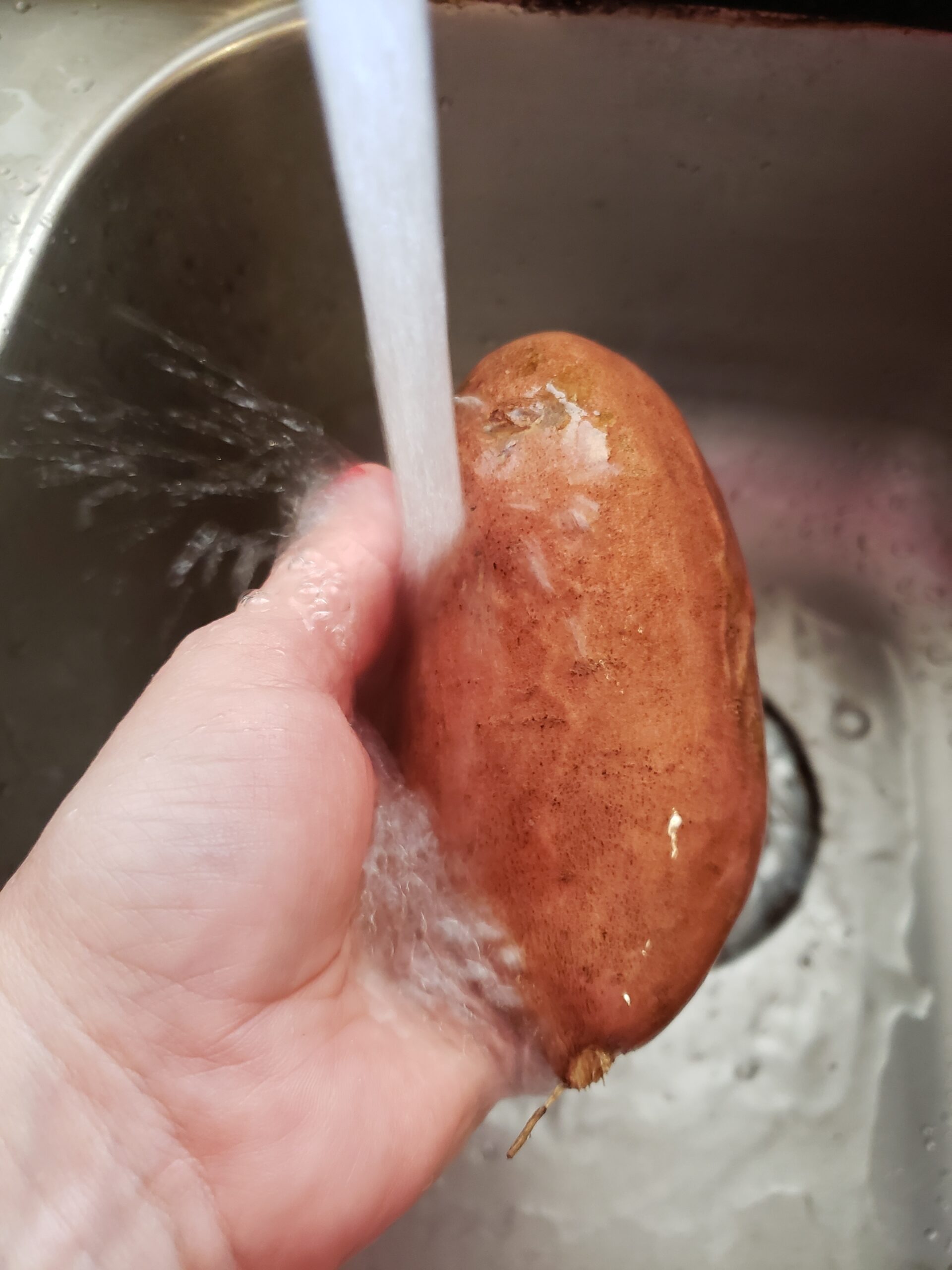washing a sweet potato under running water