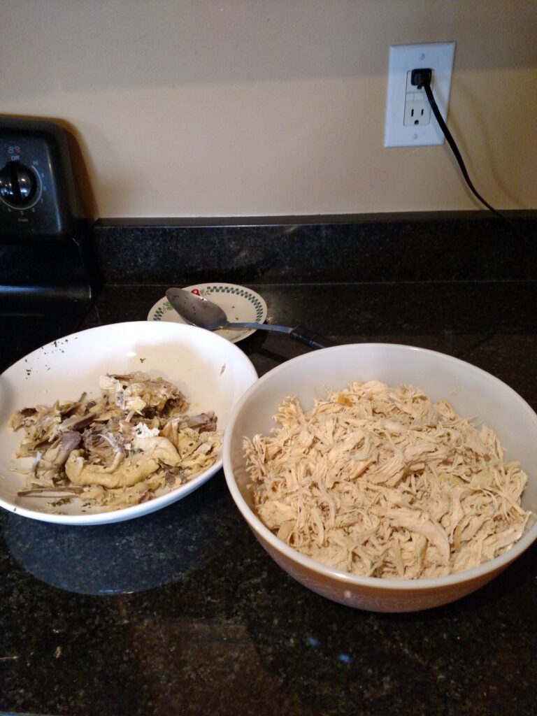 shredded chicken in large bowl on right and skin and bones on plate on the left