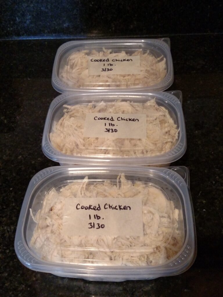 cooked shredded chicken in 3 containers labeled and ready for the freezer