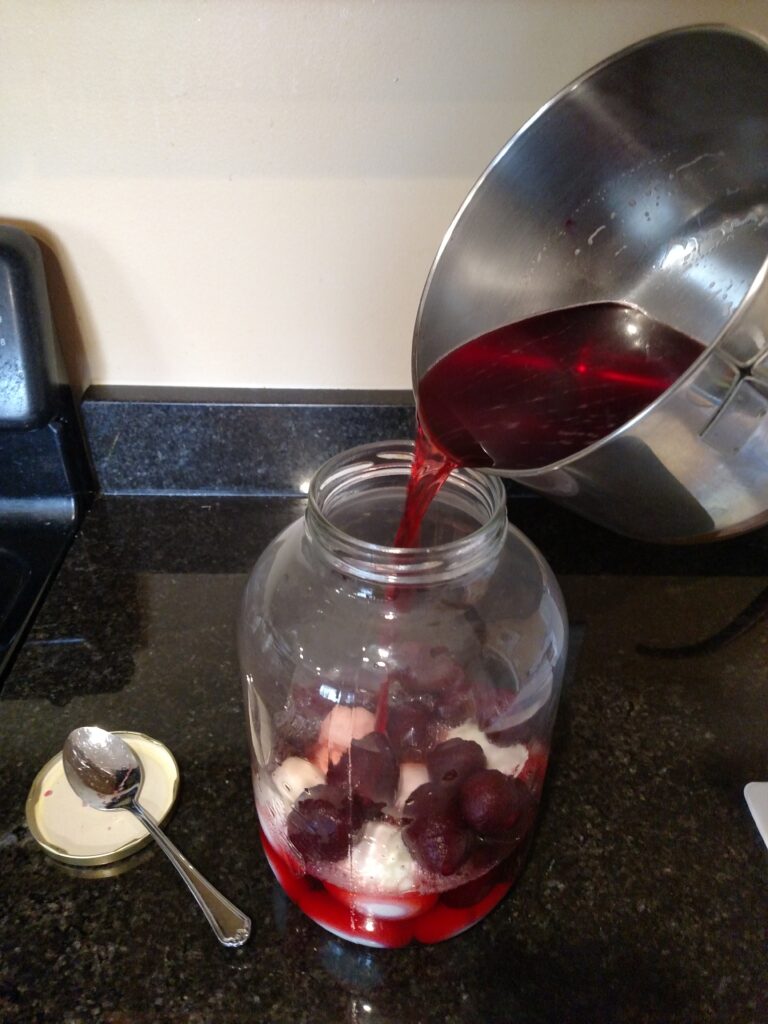 pouring beet juice and vinegar mixture to glass jar of hardboiled eggs and beets