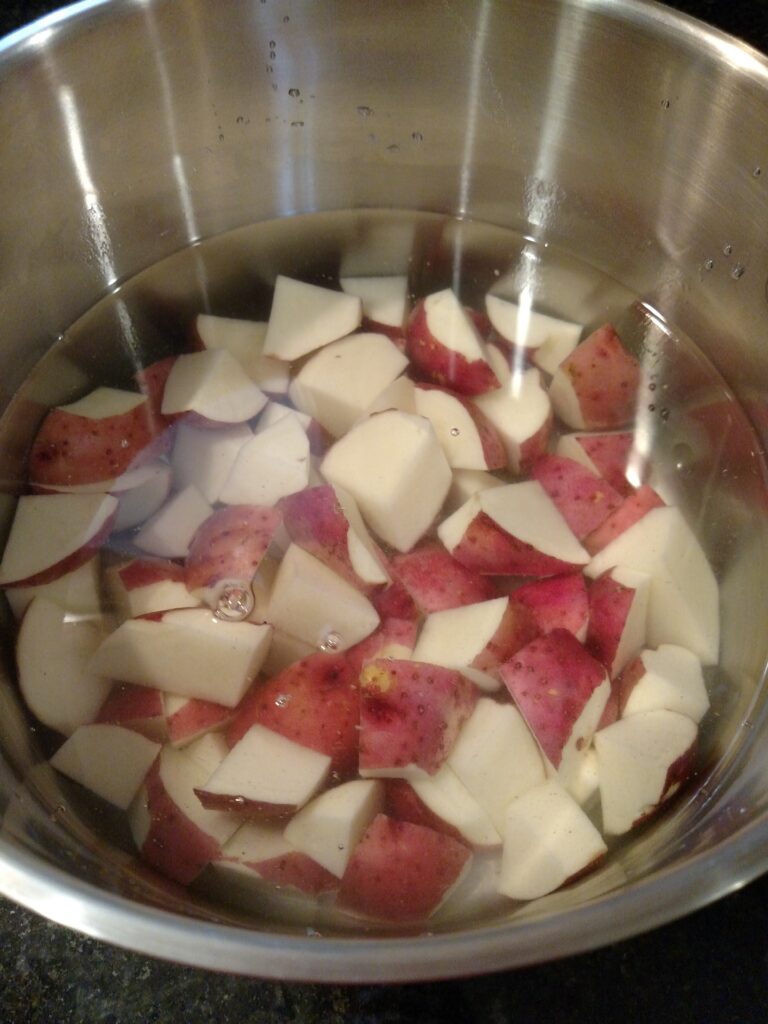 red potatoes cut and in water in saucepan on stove