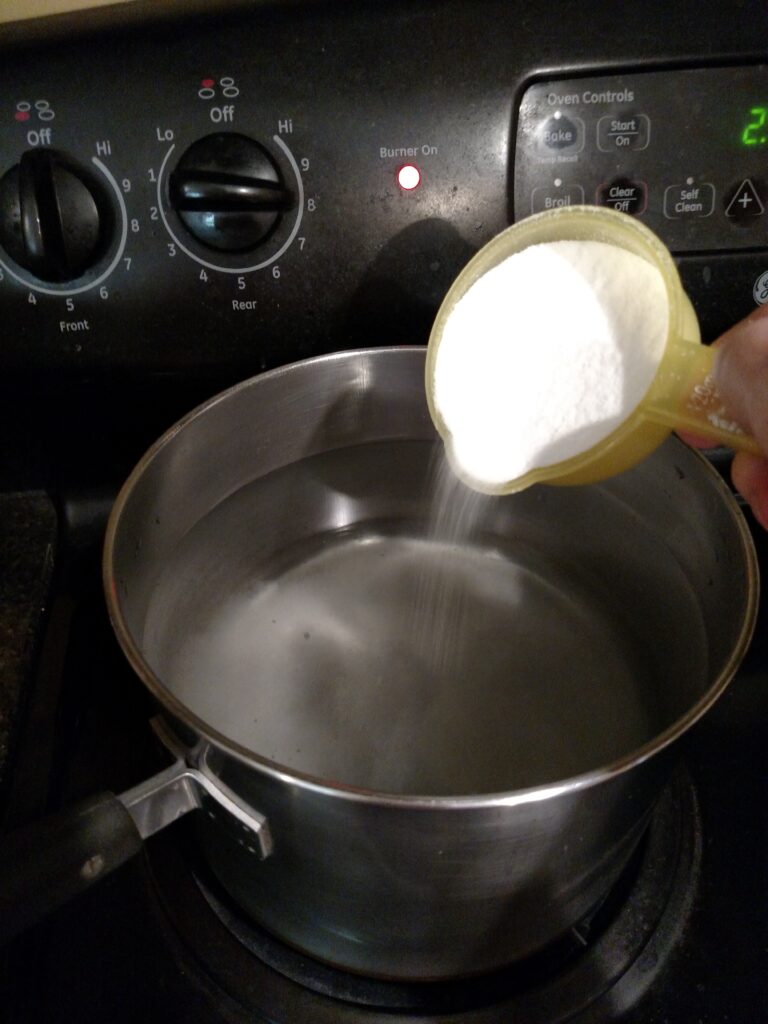 adding sugar to water in saucepan on stove for peach syrup