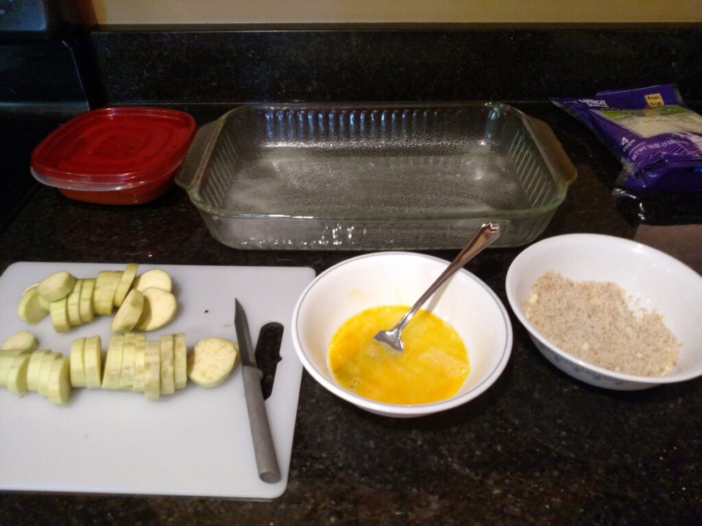 sliced eggplant on left, bowl with egg in middle, bowl with breading on right.