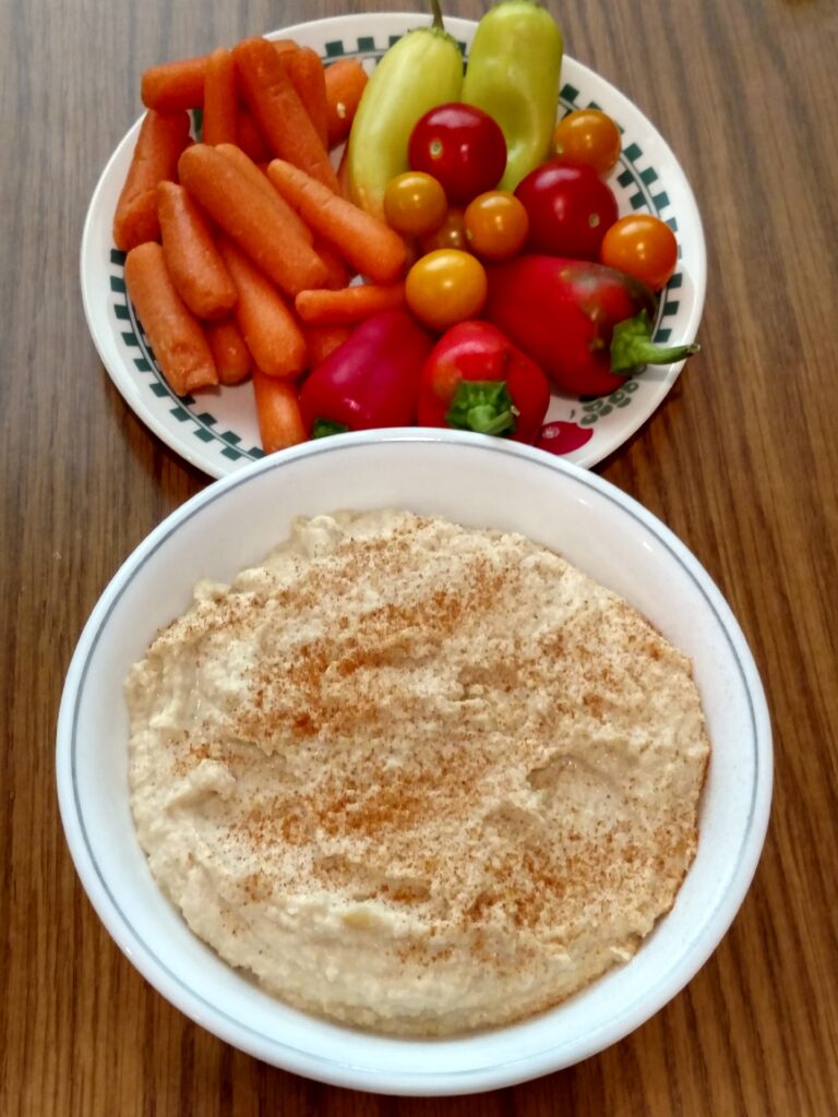 homemade hummus in bowl next to plate of vegetables for dipping