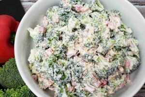 broccoli salad in white bowl next to red pepper and broccoli