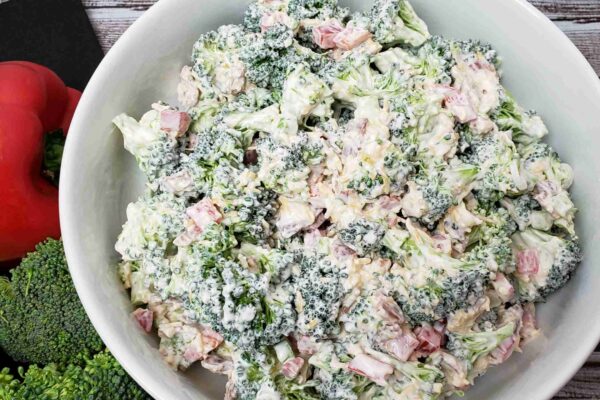 broccoli salad in white bowl next to red pepper and broccoli