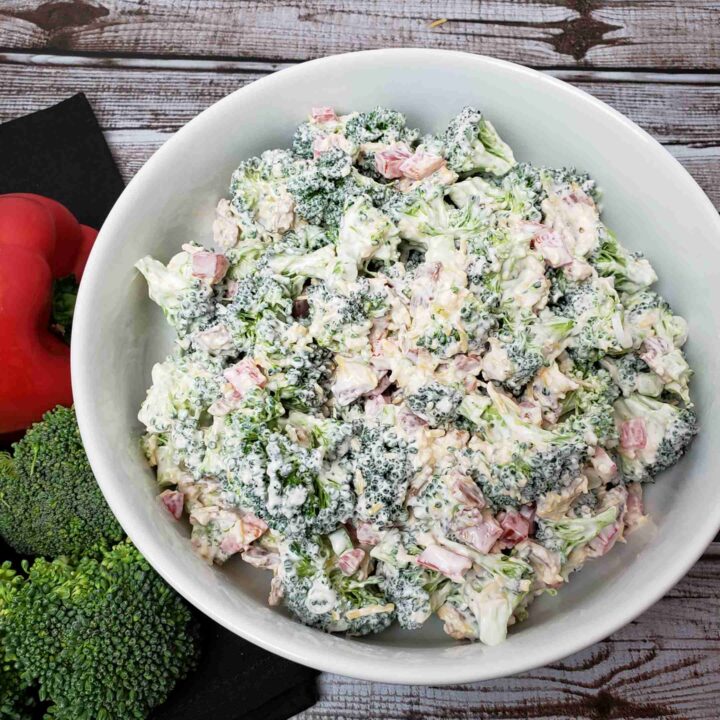 broccoli salad in white bowl next to red pepper and broccoli