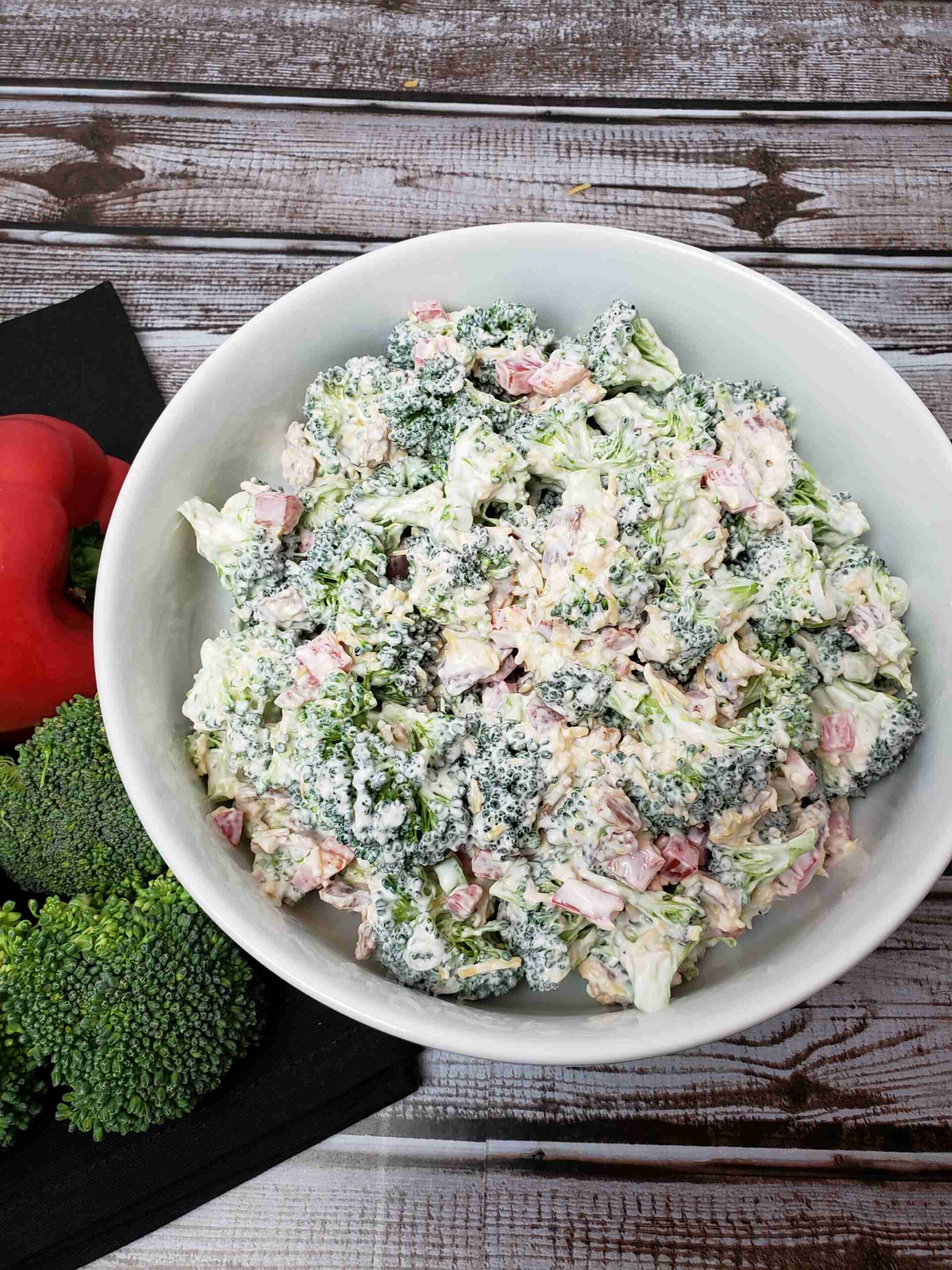 broccoli salad in white bowl next to red pepper and broccoli