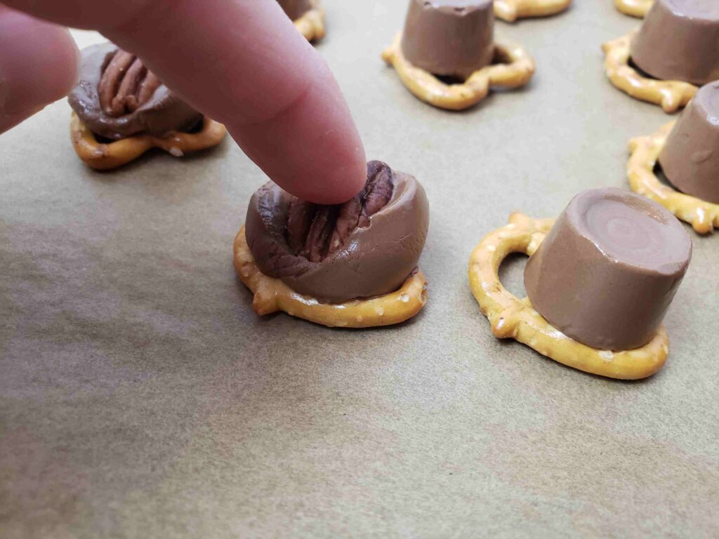 pressing pecan into rolo candy on pretzels